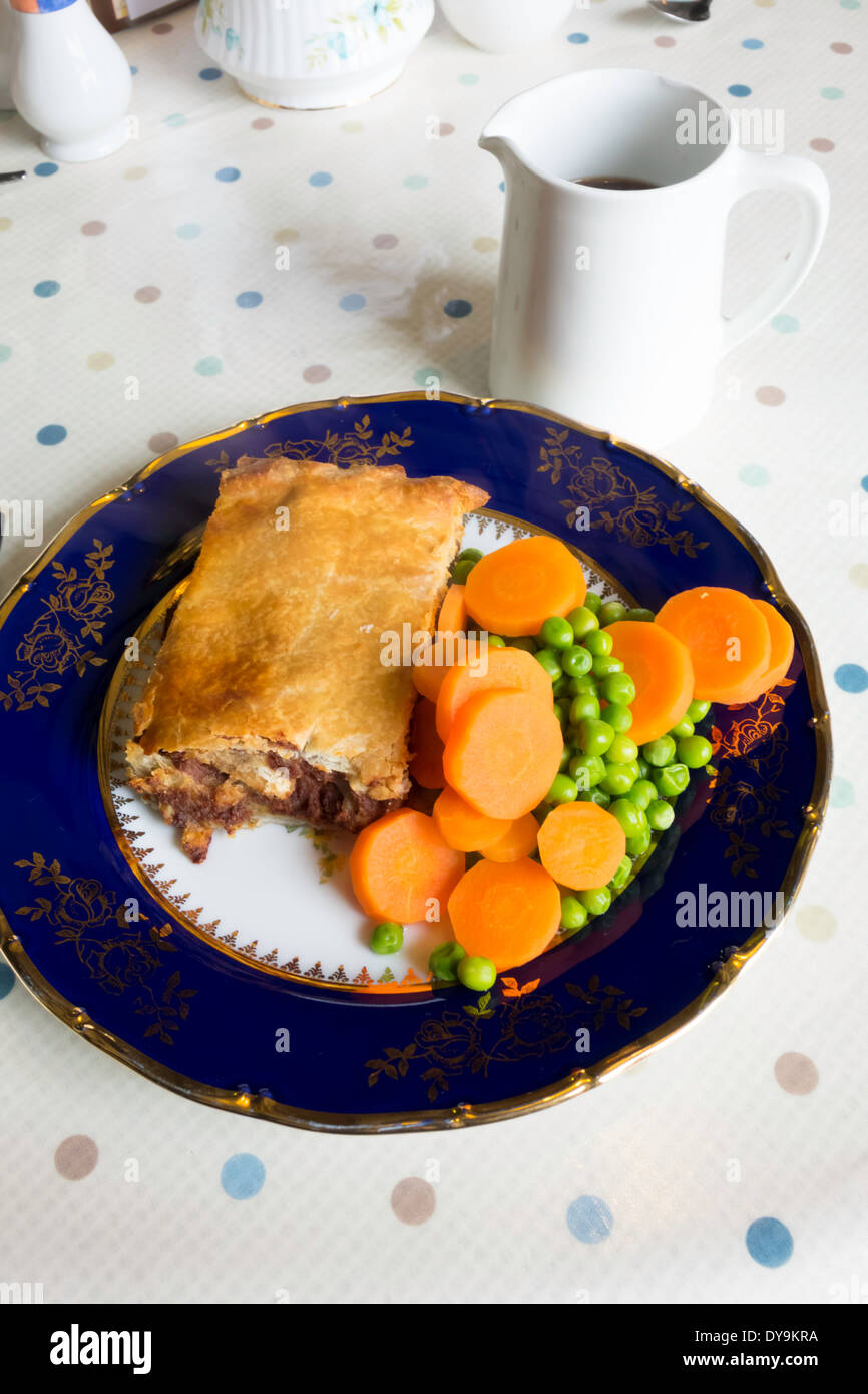 English lunch time snack, a corned beef and potato pie with carrots peas and a jug of gravy on a blue and gold china plate Stock Photo