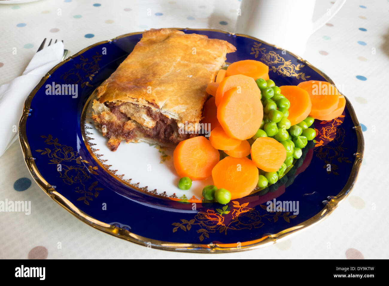 English lunch time snack, a corned beef and potato pie with carrots peas and a jug of gravy on a blue and gold china plate Stock Photo