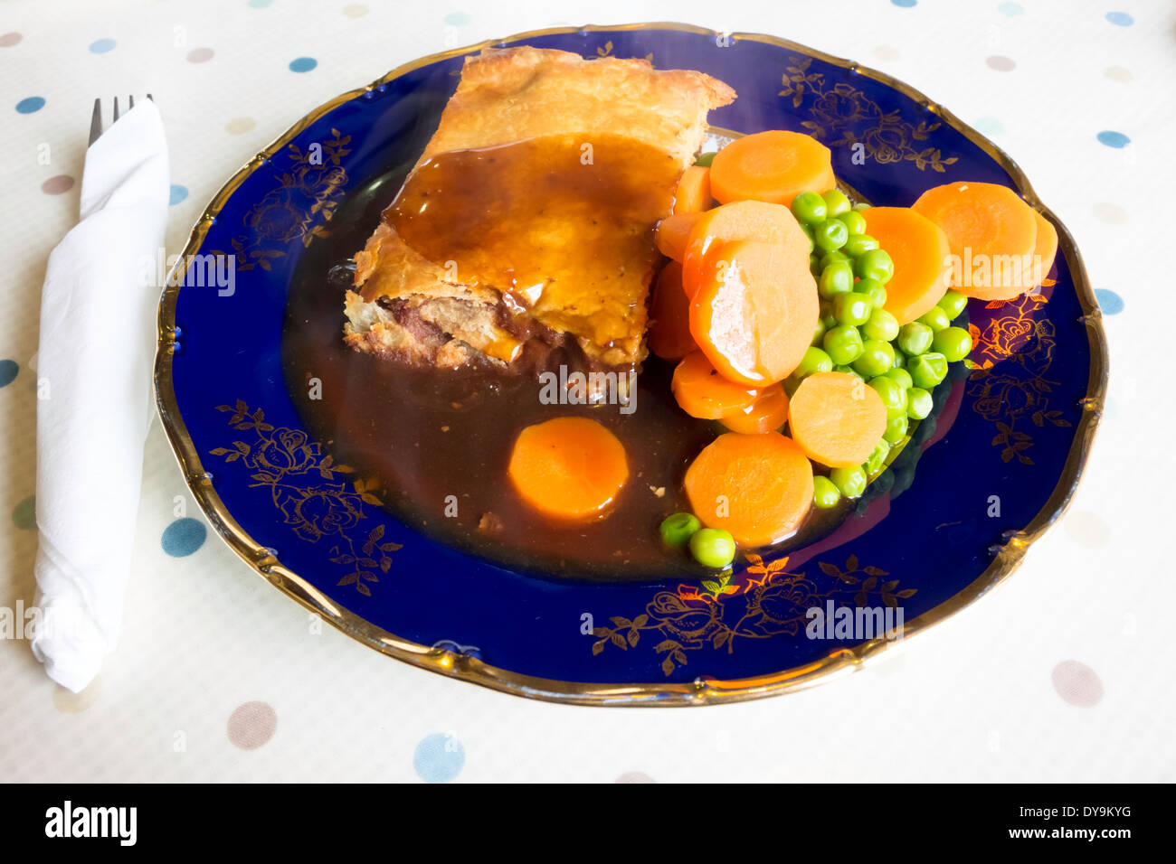 English lunch time snack, a corned beef and potato pie with carrots peas and gravy on a blue and gold china plate Stock Photo
