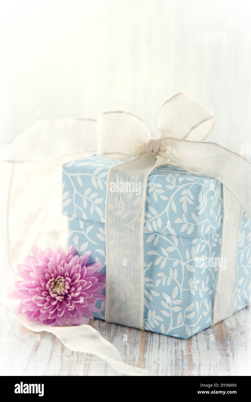 Light blue floral gift box tied up with white ribbon and pink flower on rustic wooden background and texured vintage editing Stock Photo
