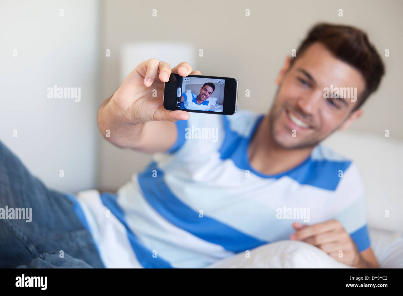 Young man reclining on bed taking selfie with smartphone Stock Photo