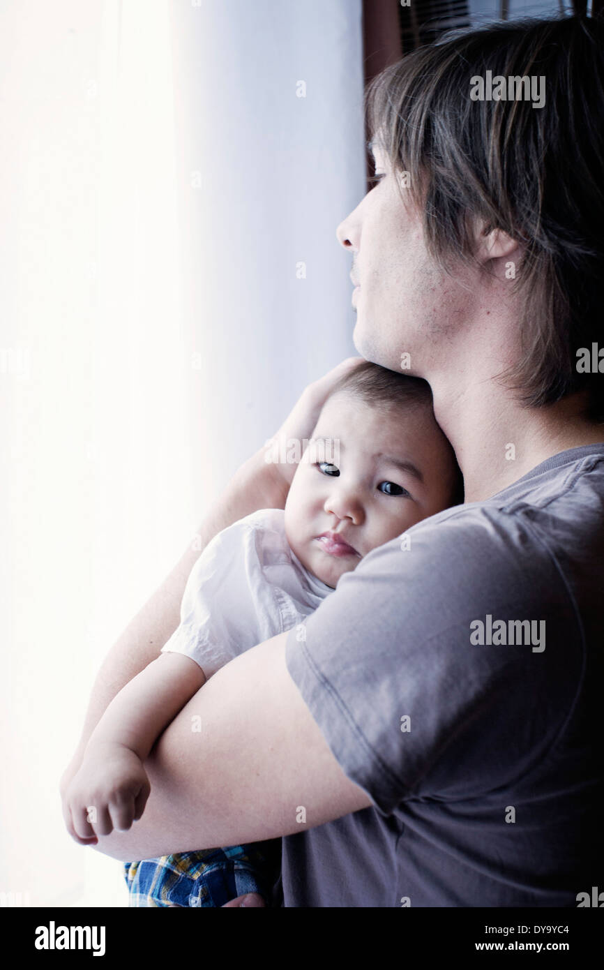 Father holding baby, looking out window Stock Photo