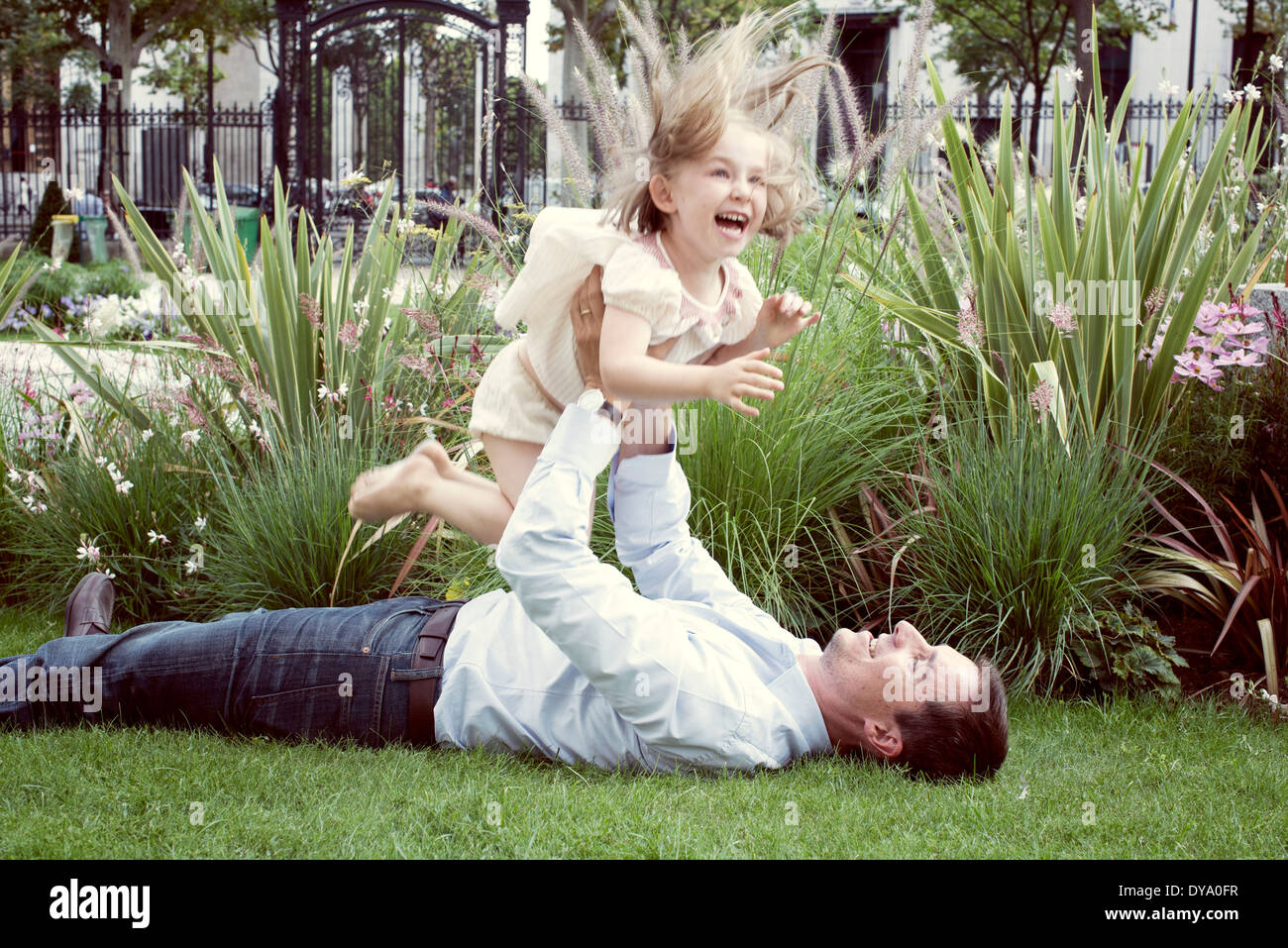 Father lying on grass, playfully lifting young daughter in air Stock Photo