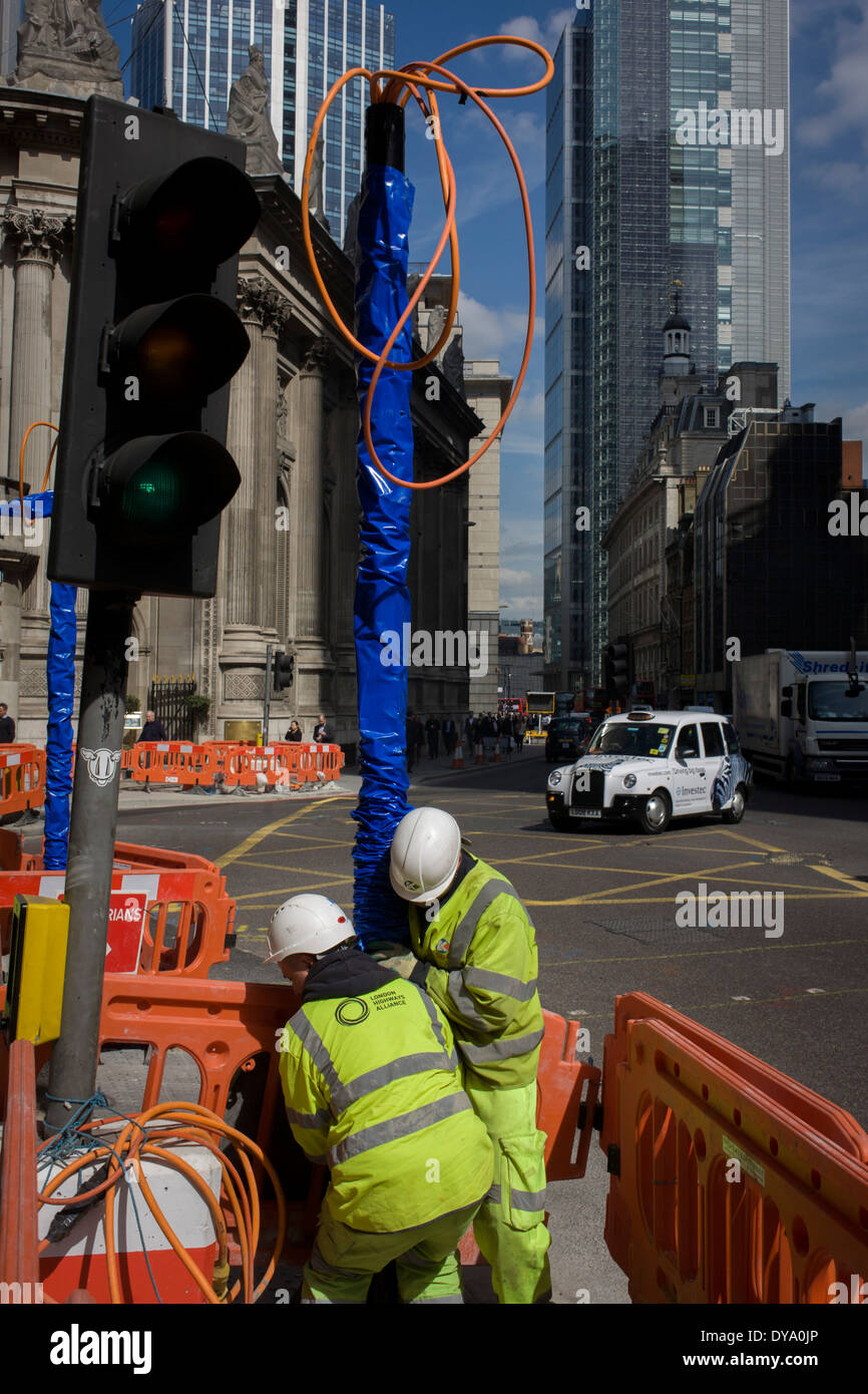 Two construction workmen manhandle a new post on Bishopsgate (Street) in the City of London, the capital's financial district. Stock Photo