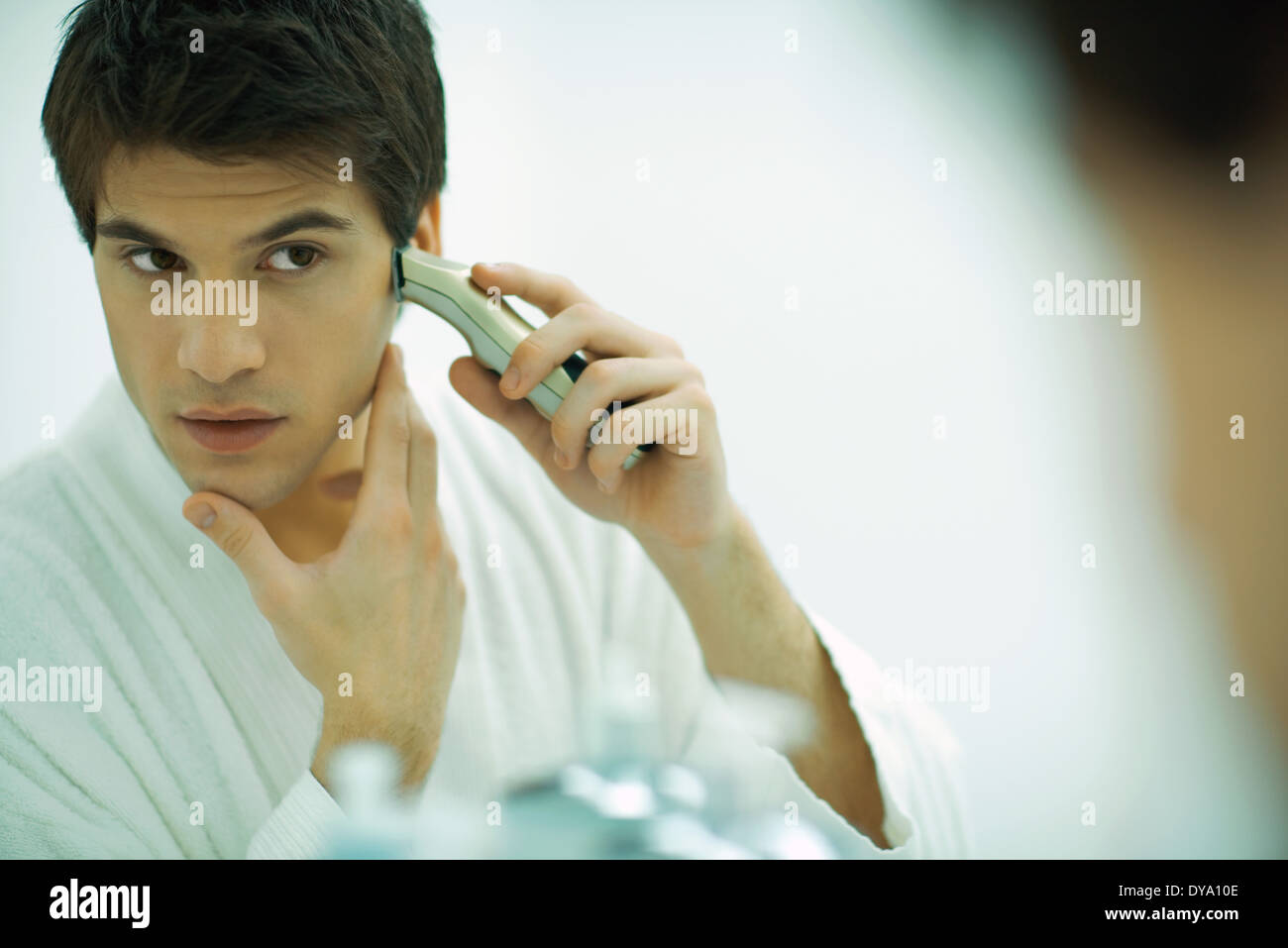 Young man looking in mirror, shaving with electric razor Stock Photo