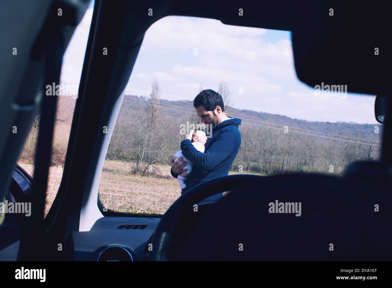 Father holding baby, viewed through car windshield Stock Photo