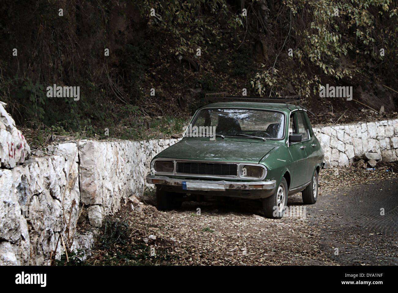 An old green car parked on the side of the road near trees. Stock Photo
