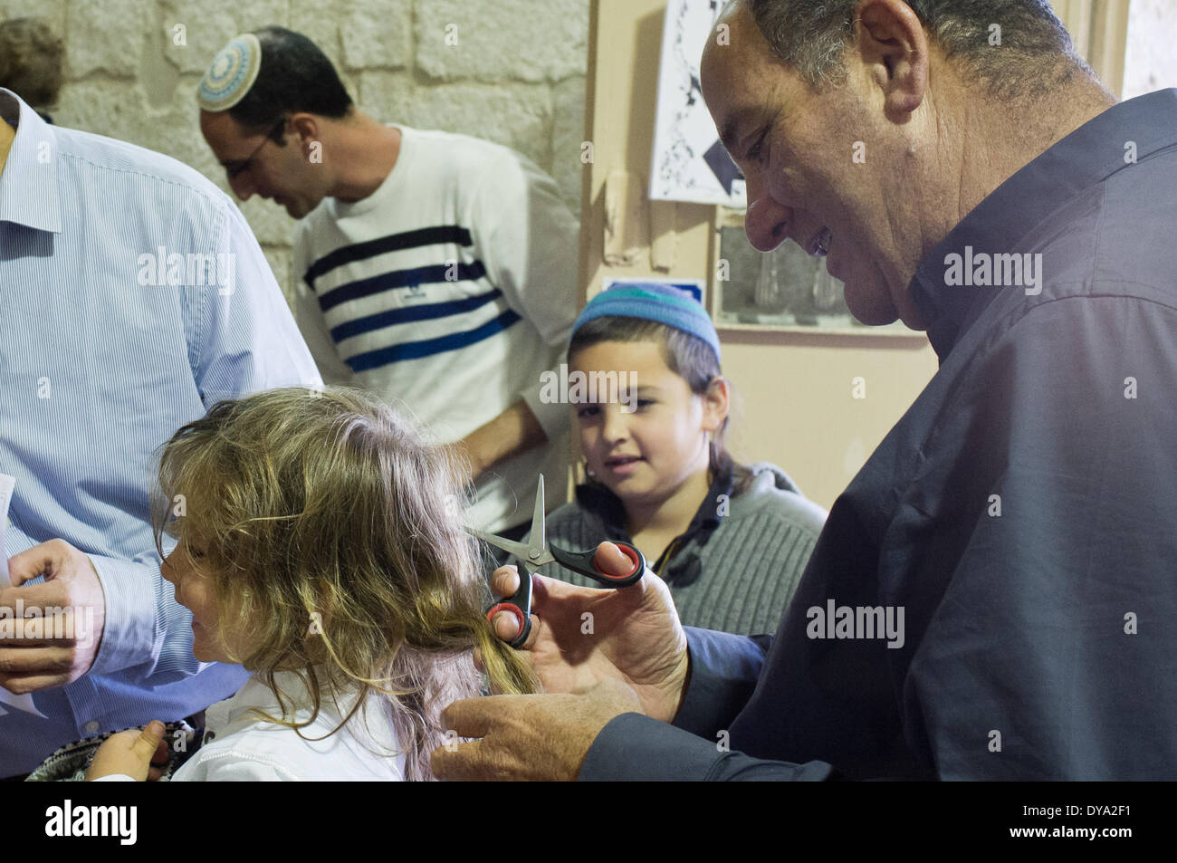 A family performs a Halaqah (Sephardic Jews) or Upsherin (Ashkenazi Jews) ceremony at the tomb of the Prophet Samuel, cutting their three-year-old son's hair for the first time. This is the traditional burial site of the biblical Prophet Samuel, just north of Jerusalem. The tomb is located in an underground chamber inside a small synagogue in the 18th century Nabi Samwil Mosque, built on the remains of a Crusader-era fortress. Stock Photo