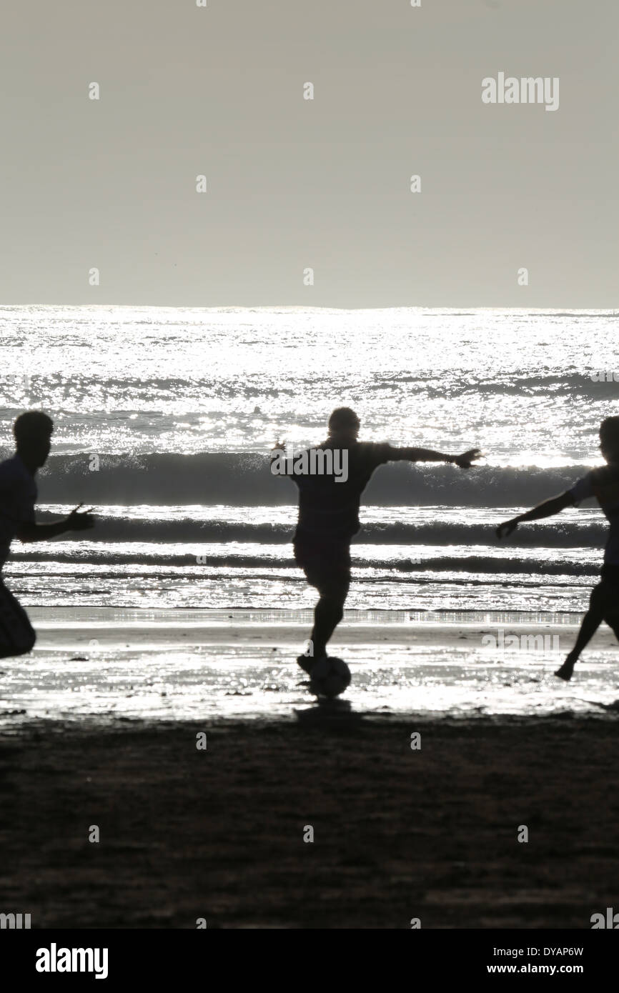Kids playing football on a beach in Essaouira, Morocco one late evening with the sea illuminated by sunshine casting a glow 1of4 Stock Photo