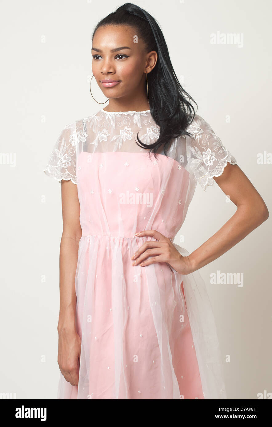 A black hair woman with ponytail, African American female model wearing a 50s pastel pink lace formal dress posing Stock Photo