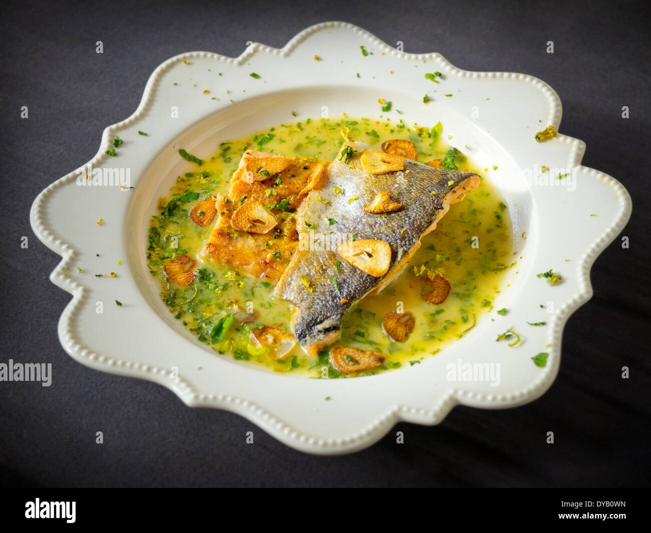 Panfried sea trout in green sauce with fried garlic slices Stock Photo