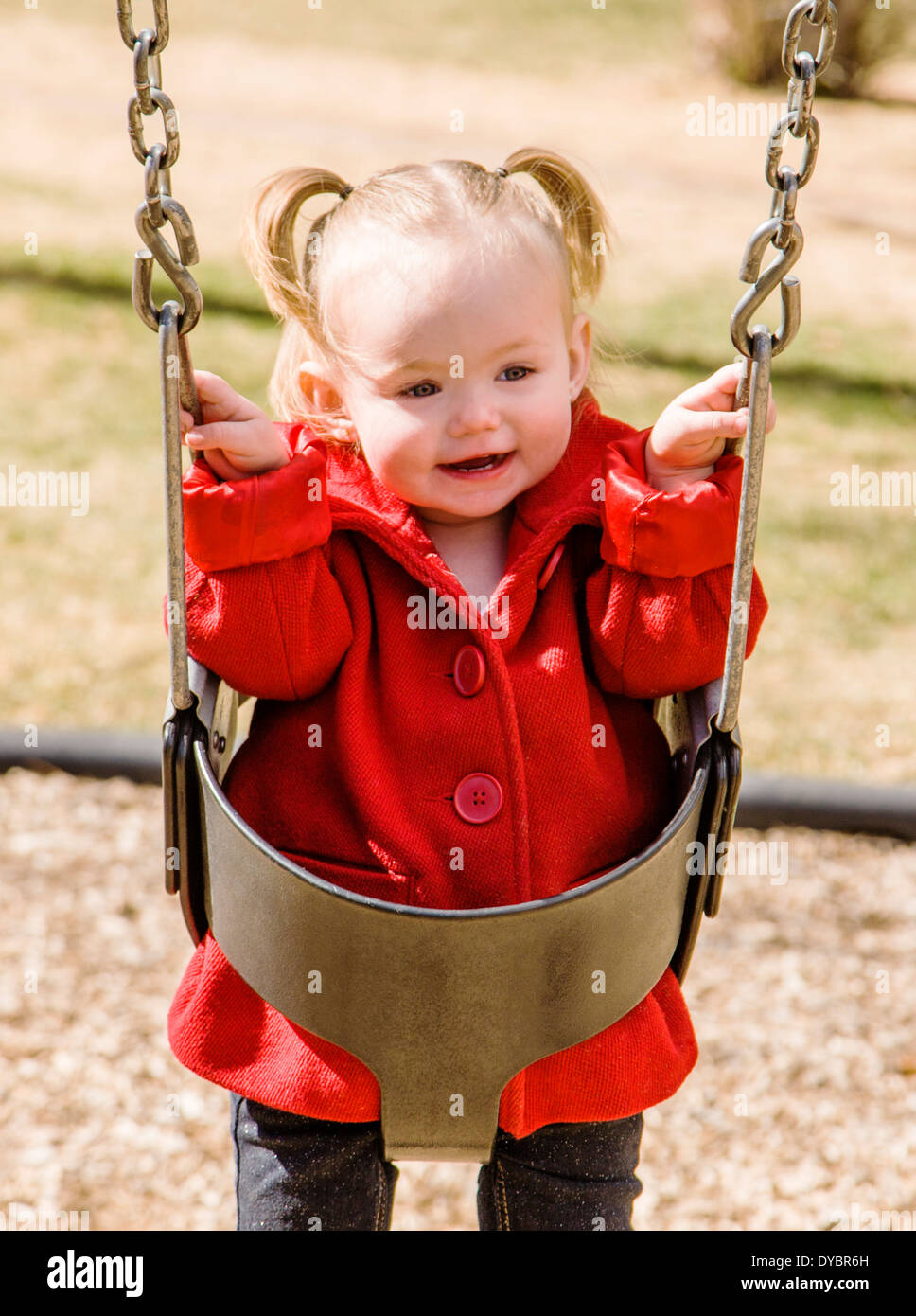 Cute, adorable 16 month little girl swinging on a park playground Stock Photo