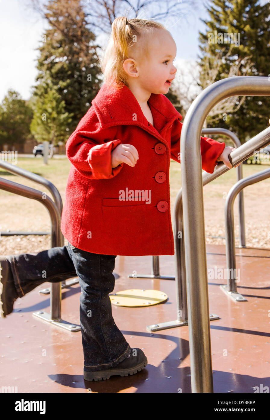 Cute, adorable 16 month little girl playing on a park playground, merry-go-round Stock Photo