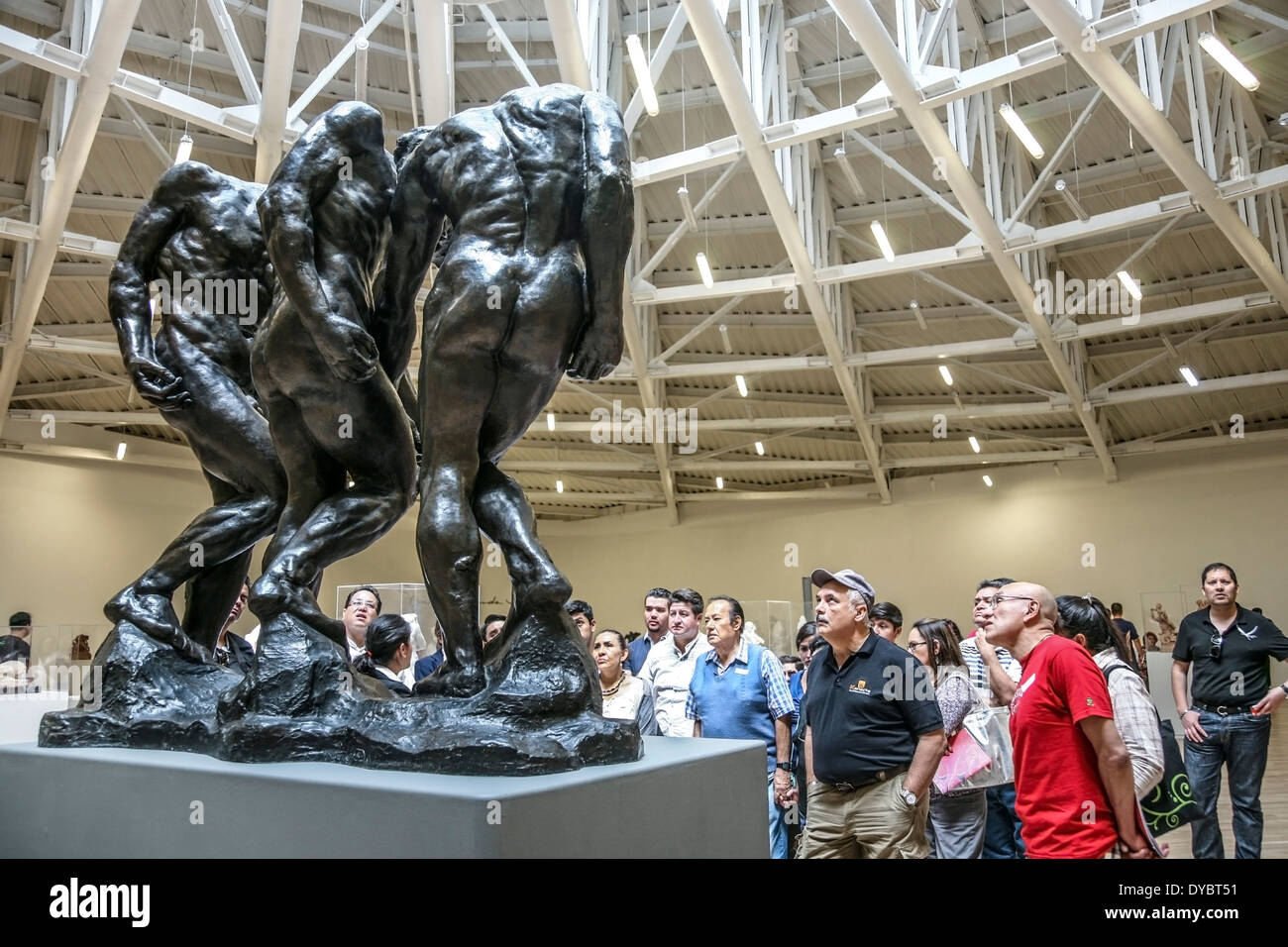 people in tour group gaze up in awe at 3 tortured figures in bronze Rodin sculpture Gates of Hell from Carlos Slim collection Stock Photo