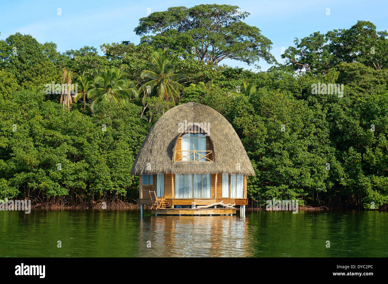 Tropical bungalow over water with thatched palm roof and lush vegetation in background, Bocas del Toro, Caribbean sea, Panama Stock Photo