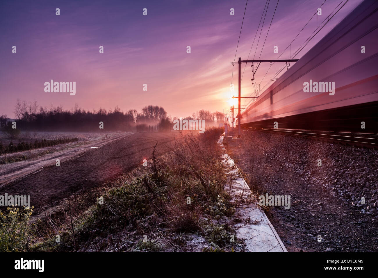 on an early morning at sunrise right next to a passing train with fog banks in the distance Stock Photo