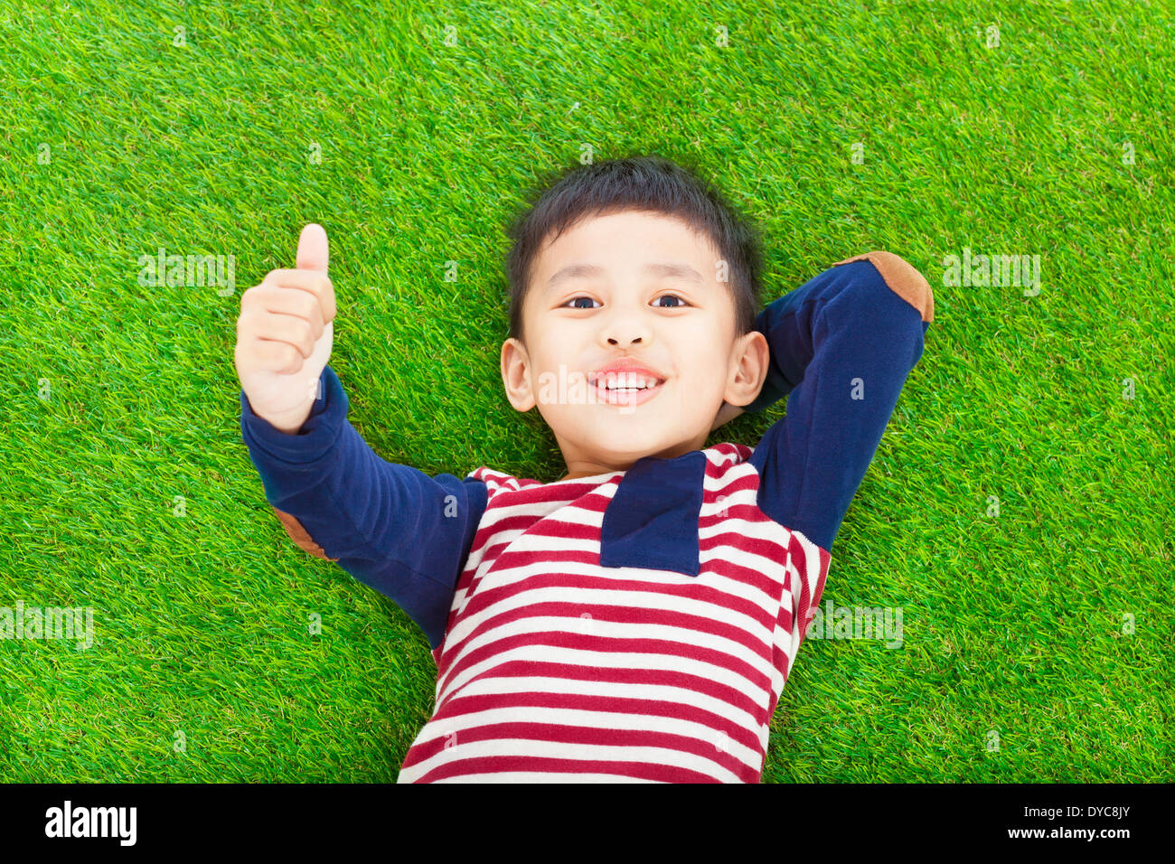 happy kid lying and raise his thumb on a meadow Stock Photo