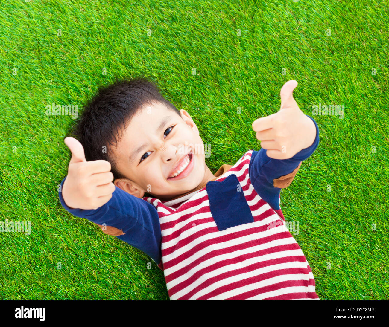 smiling kid lying and thumb up on a meadow Stock Photo