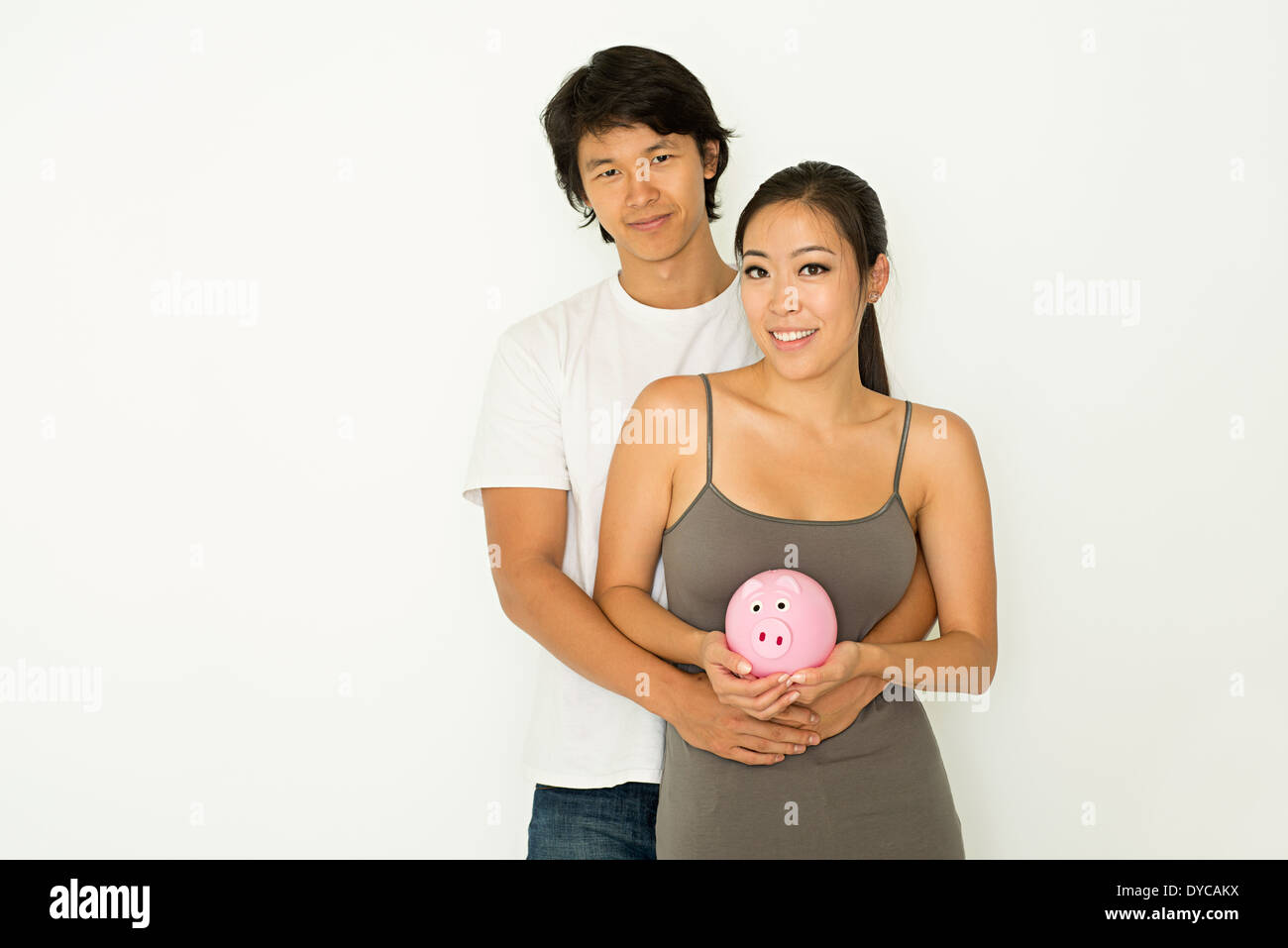 A young Asian couple stand hugging, holding a pink piggy bank, a money saving concept, couple finance planning concept. Stock Photo