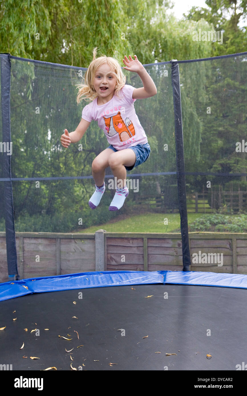 Girl aged 5- 6 on bouncing trampoline in her back garden Stock Photo