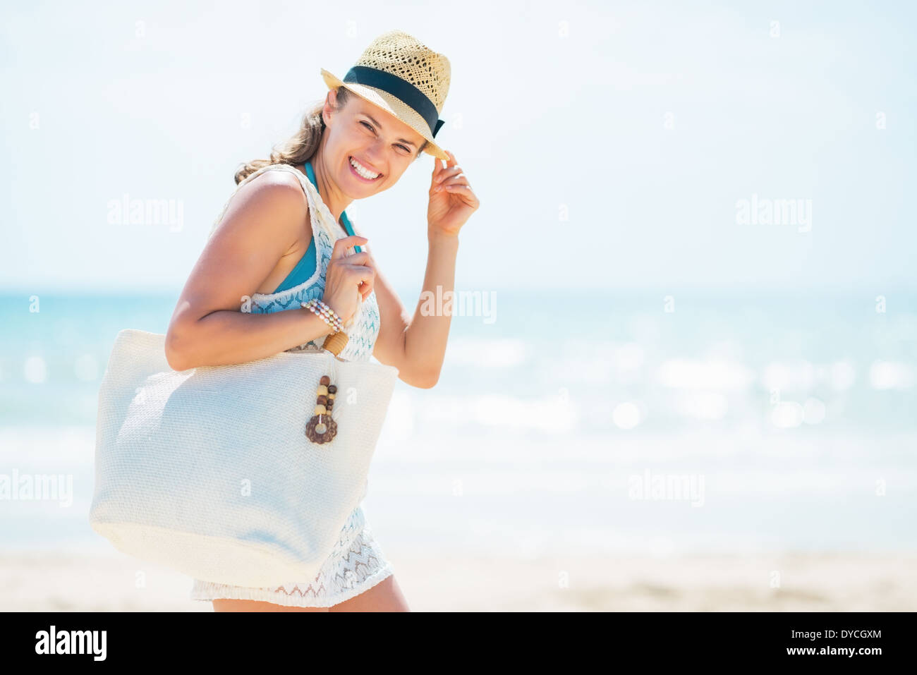 Portrait of smiling young woman in hat with bag on beach Stock Photo ...