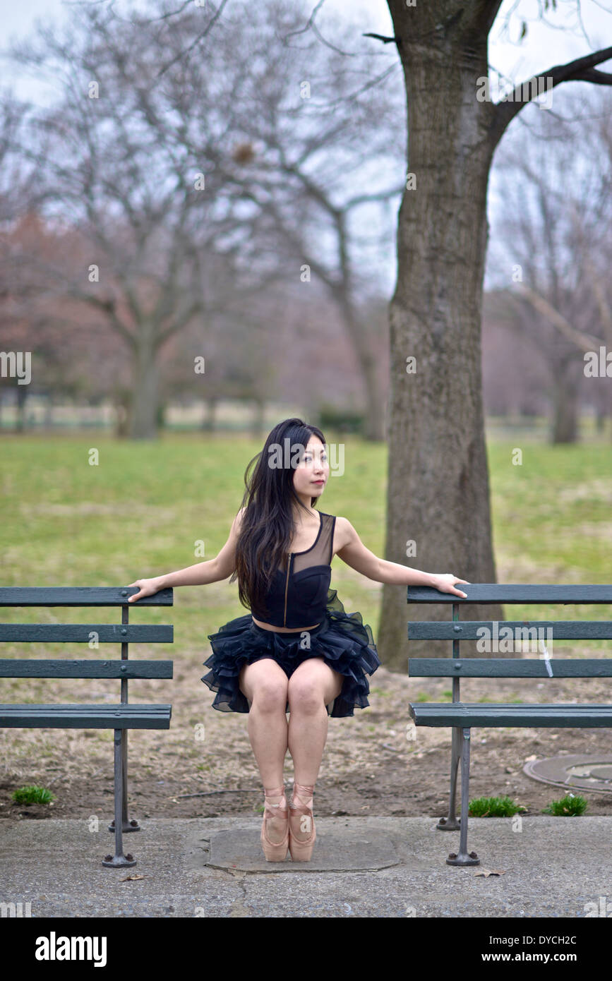 Asian ballerina wearing a black tutu sitting on the air between two park benches Stock Photo
