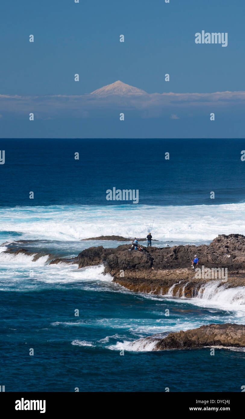People fishing on the north coast of Gran Canaria with snow capped volcano, El Teide on Tenerife in distance. Canary Islands. Stock Photo