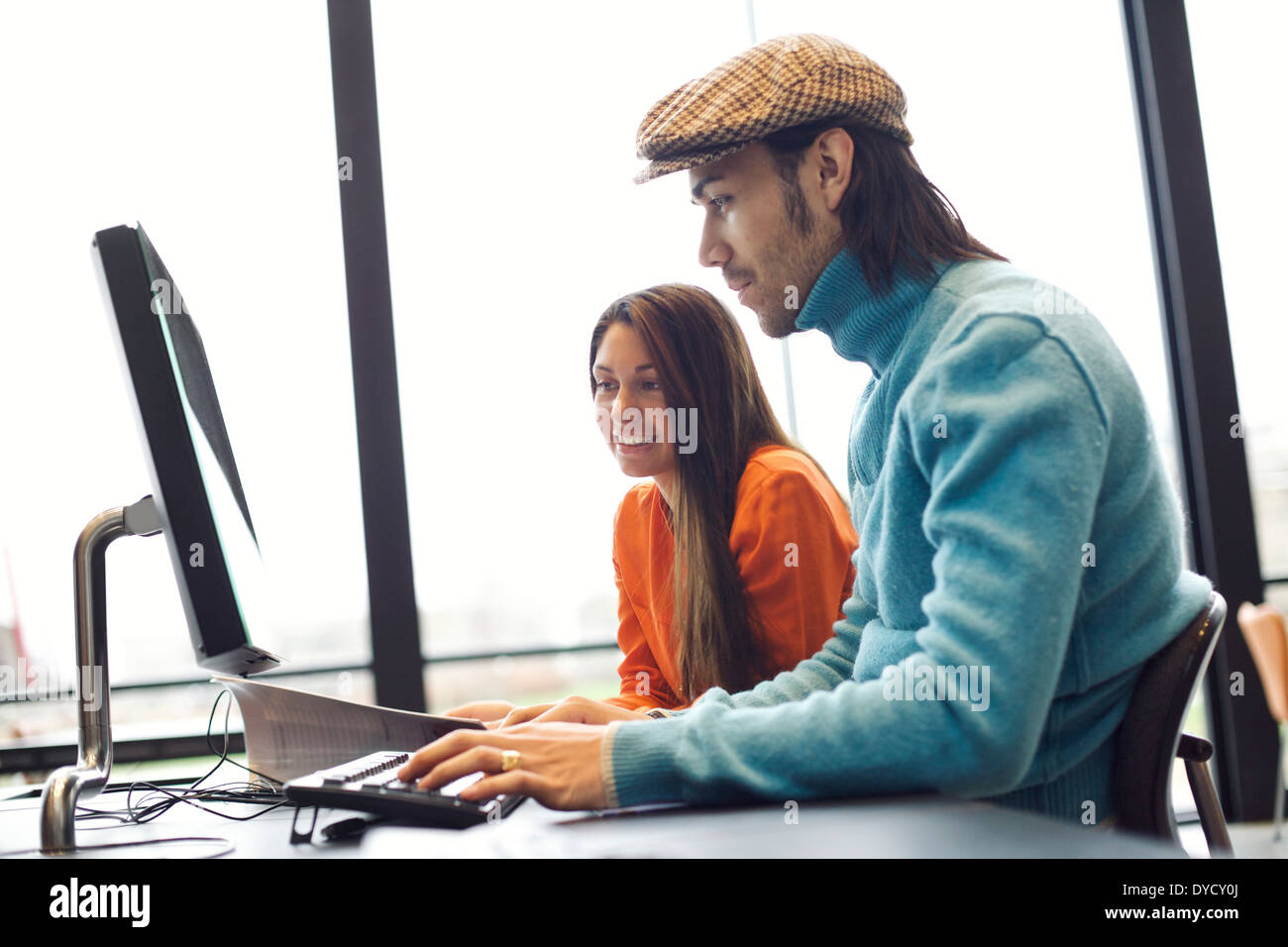 Two young people finding information on internet for their academic project. Students sitting at table with book and computer. Stock Photo