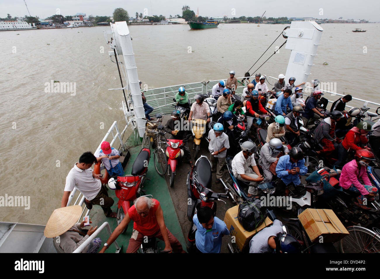 People sit on their motorcycles onboard a ferry crossing the Mekong ...