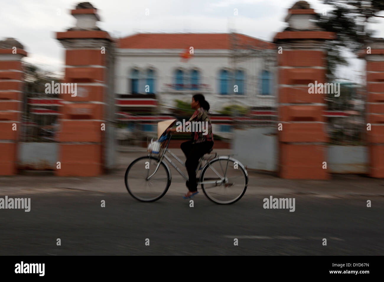 A woman bikes past the governor's office in Ben Tre province, Vietnam Stock Photo