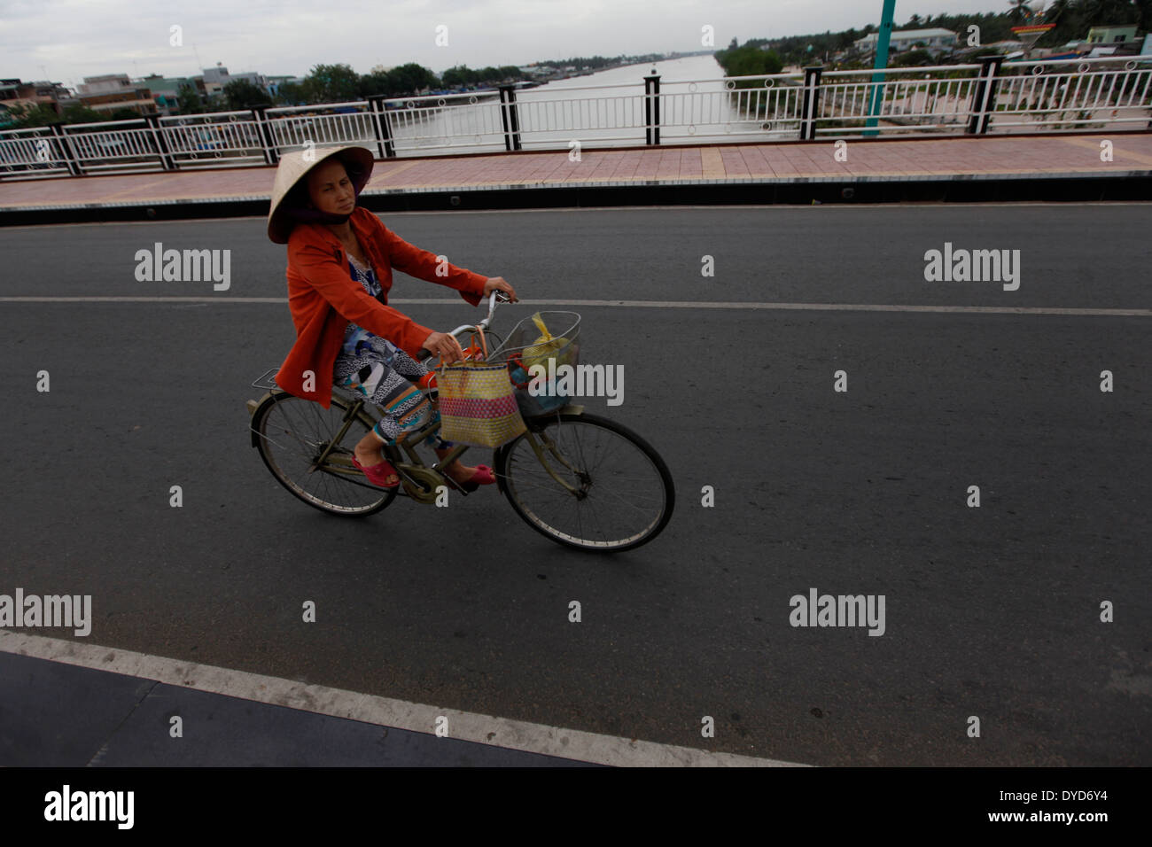 A woman rides her bicycle across a bridge in Ben Tre province, Vietnam Stock Photo