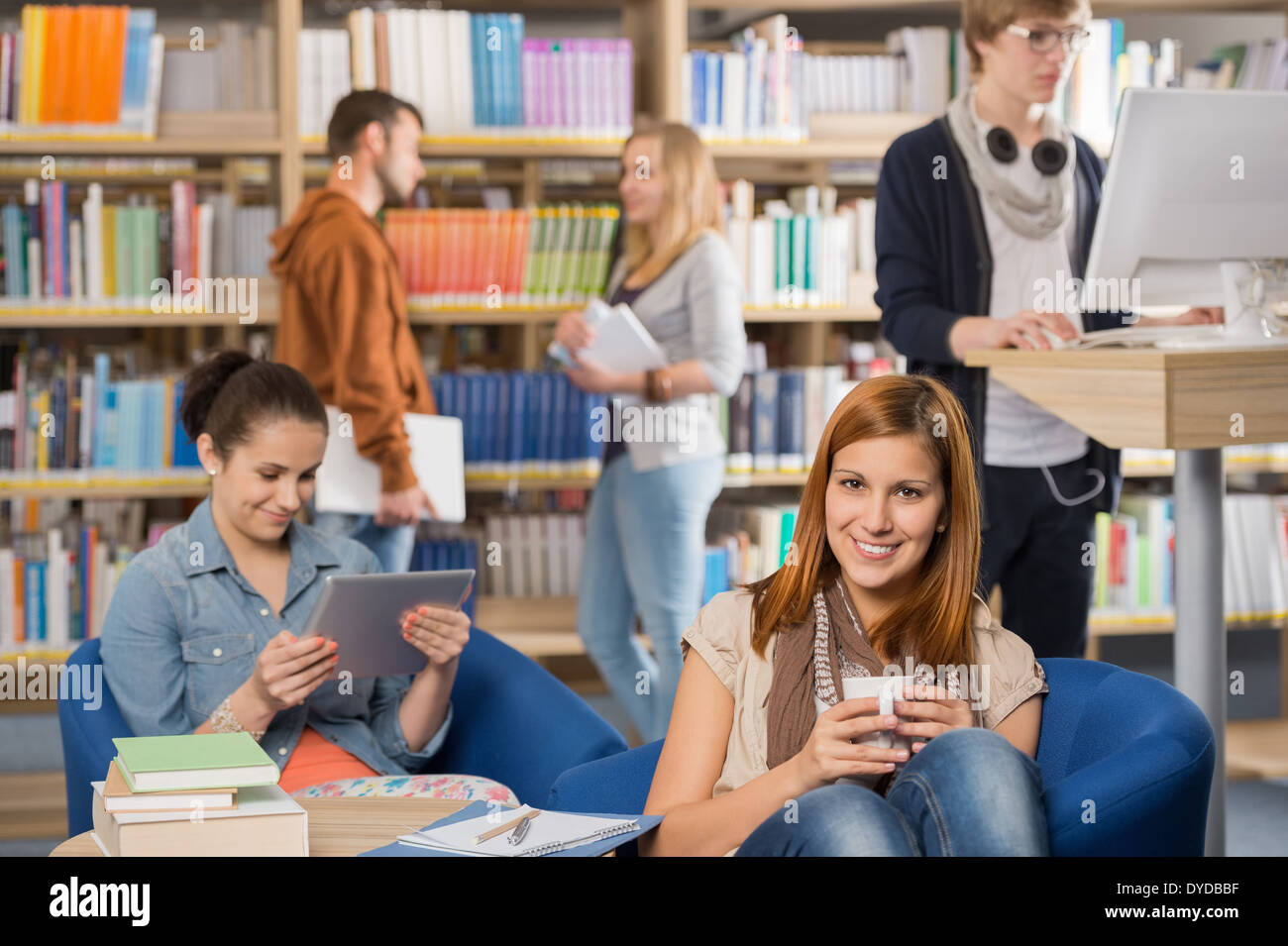 Smiling girl having coffee with students in background at library Stock Photo