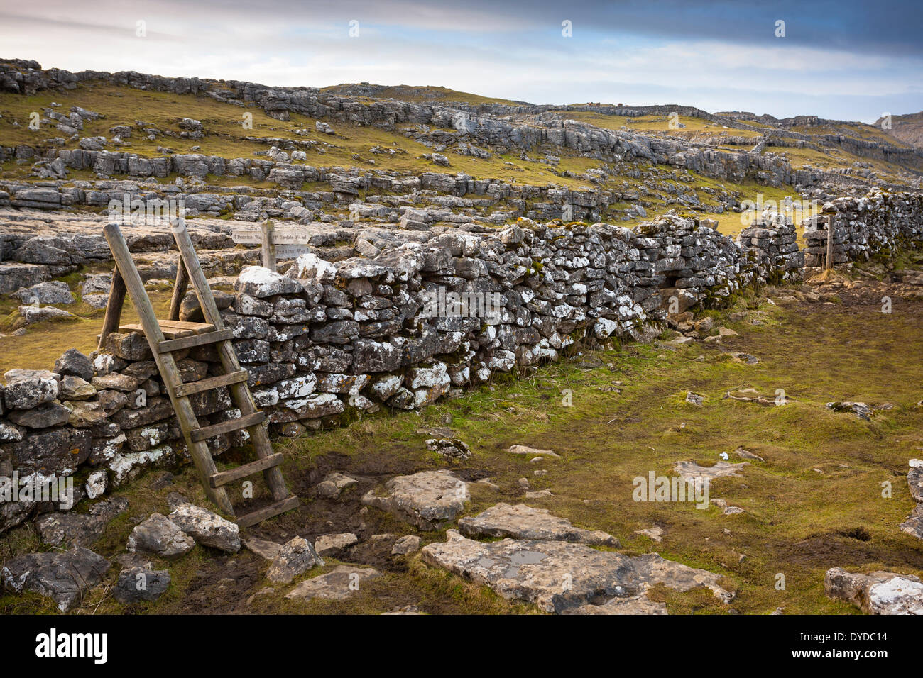 A wooden stile over a stone wall in the Yorkshire dales adjacent to a sign for the Pennine way at Malham Cove. Stock Photo