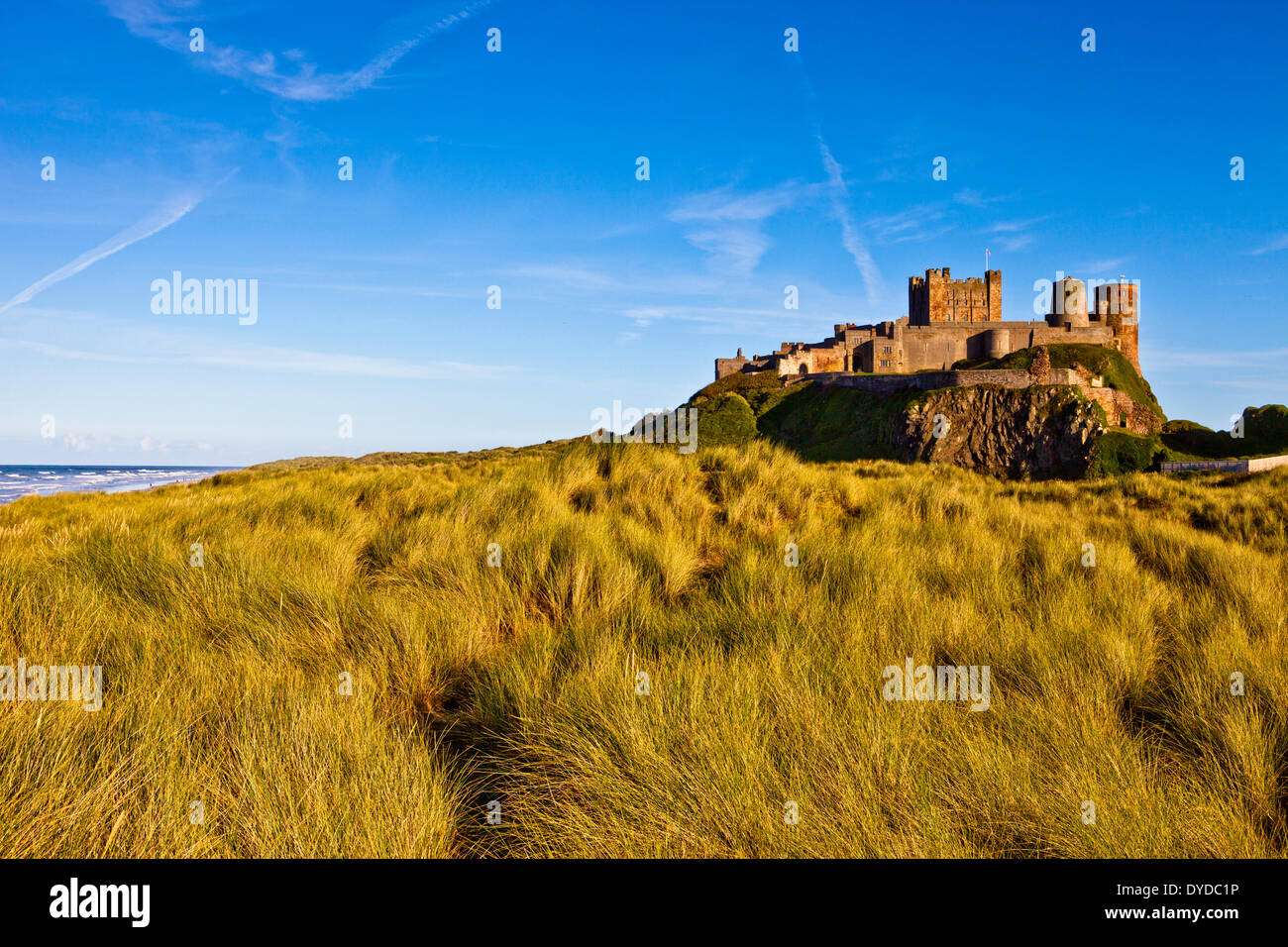 Bamburgh castle rises above the sea and dunes. Stock Photo