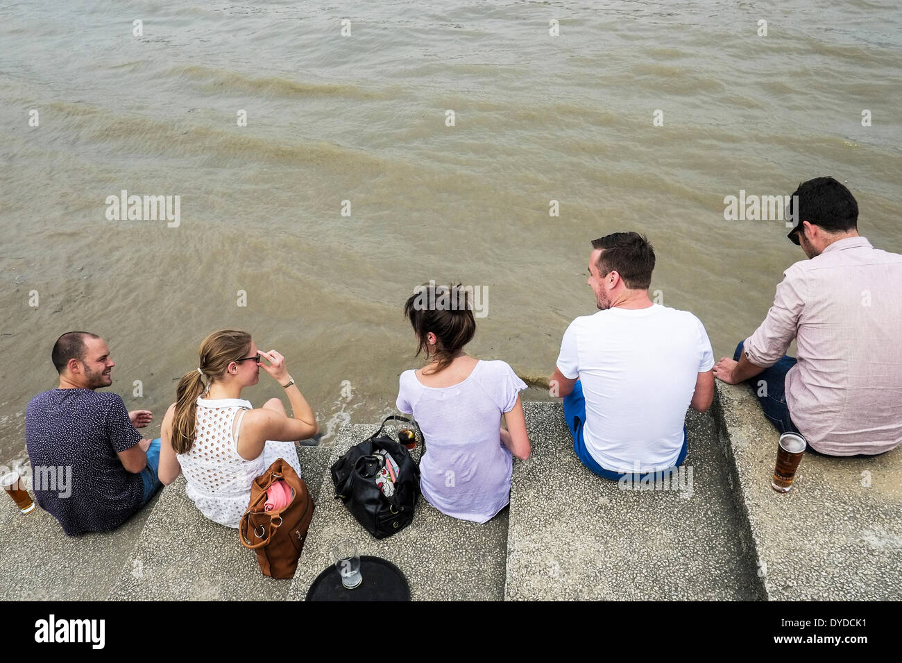 Friends sitting on steps overlooking the River Thames. Stock Photo