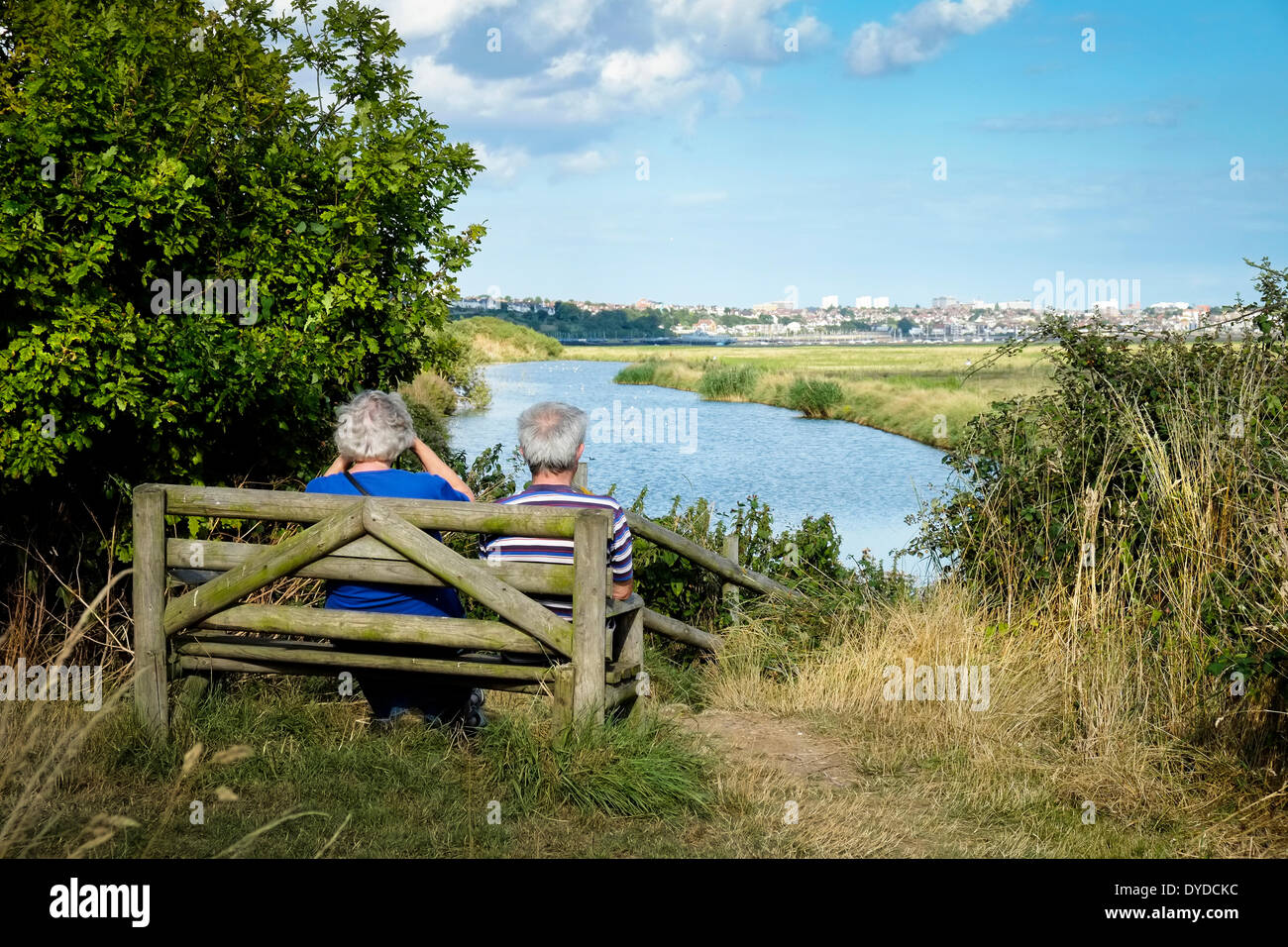 A couple sitting on a wooden bench enjoying the view over to Southend. Stock Photo