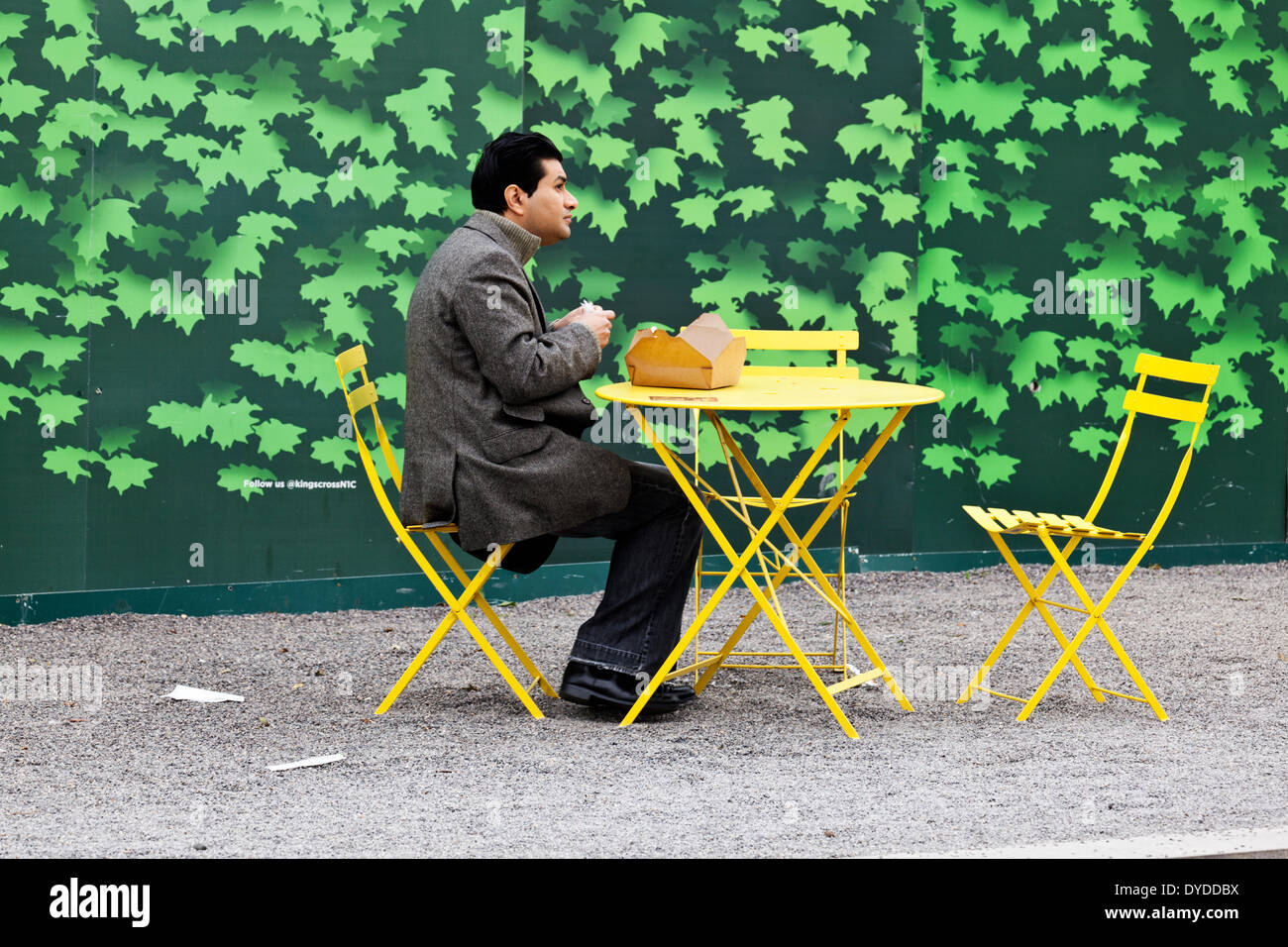 An Asian man eats takeaway in front of architectural hoardings. Stock Photo