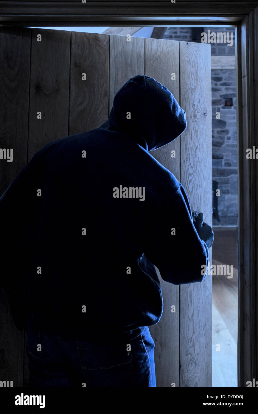 An anonymous hooded male opening a door and entering a room. Stock Photo