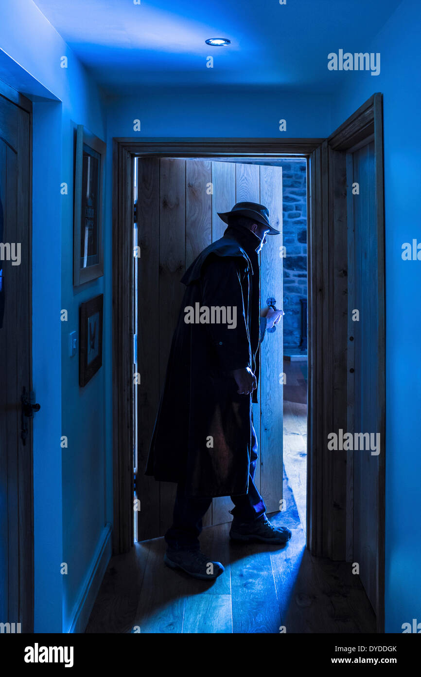 An man wearing a hat and long raincoat entering a room. Stock Photo