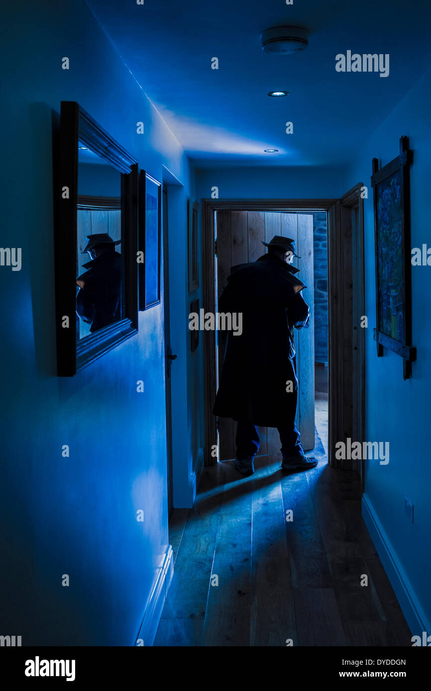 An man wearing a hat and long raincoat entering a room. Stock Photo