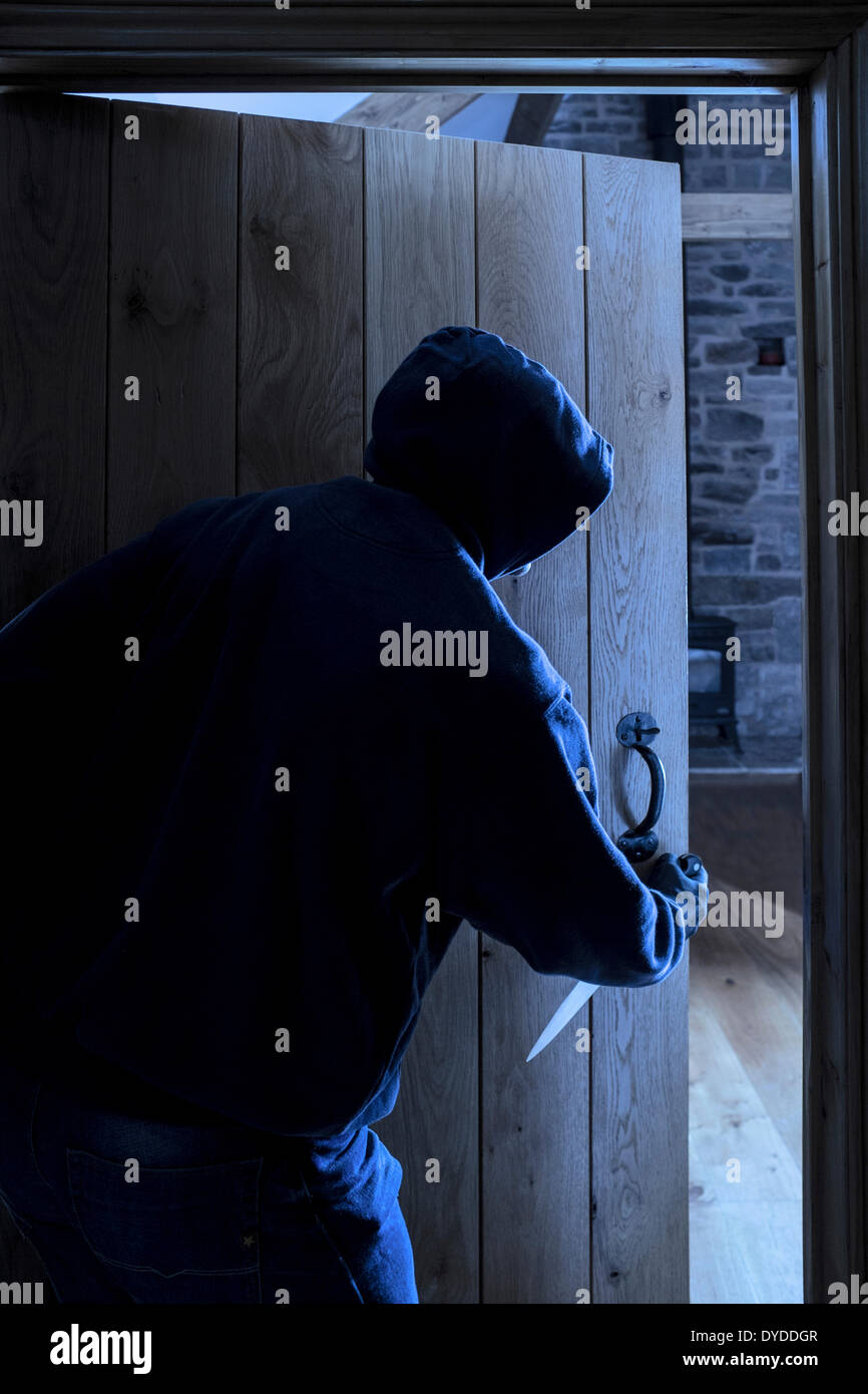 An anonymous hooded male carrying a knife entering a room. Stock Photo