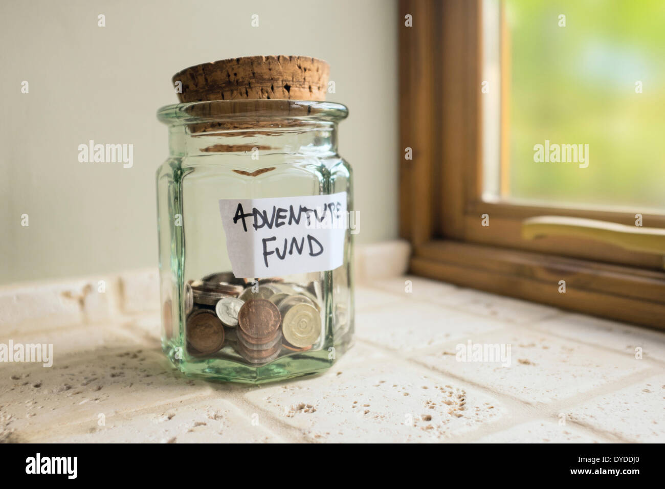 Glass jar labelled Adventure Fund containing loose change. Stock Photo