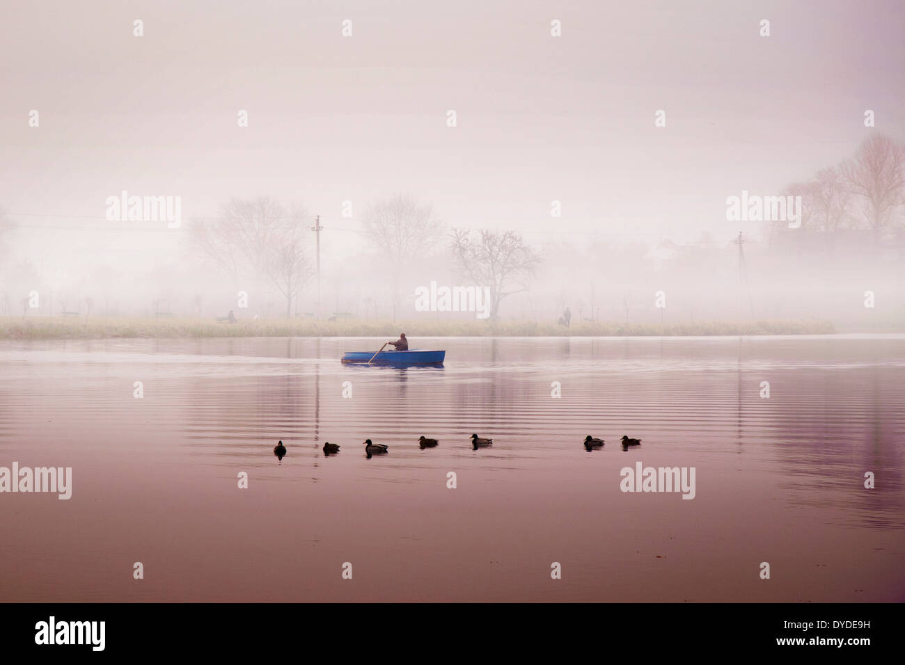 men in paddle boat travel by river in fog by warm autumn morning Stock Photo