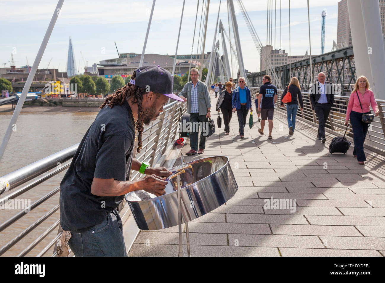 Busker playing steel band drum on the Golden Jubilee pedestrian bridge over the Thames by Hungerford Bridge. Stock Photo