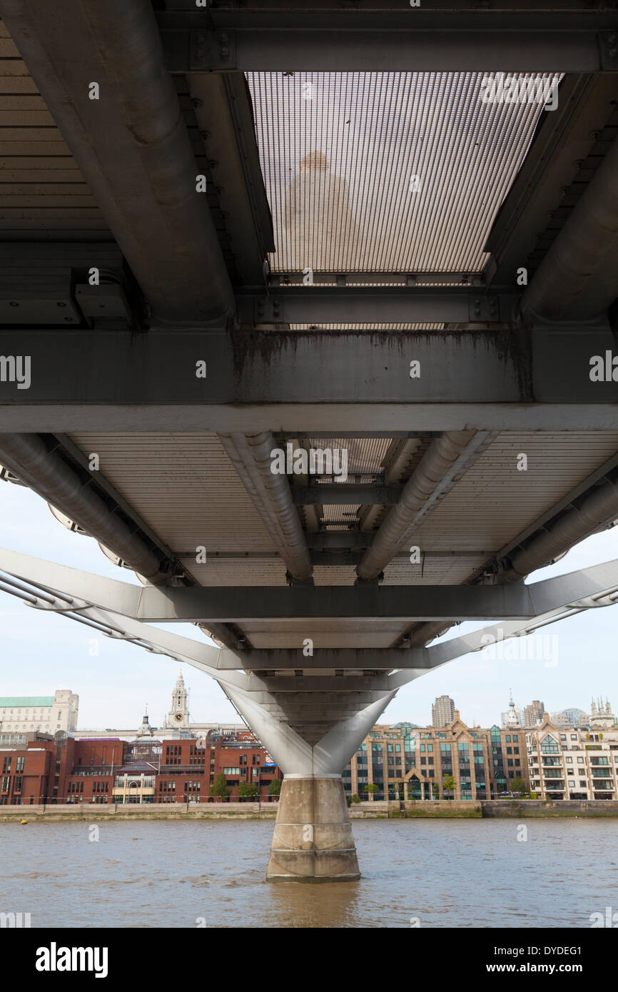 Underside of the Millennium Bridge with the River Thames and a pedestrian seen through the mesh. Stock Photo