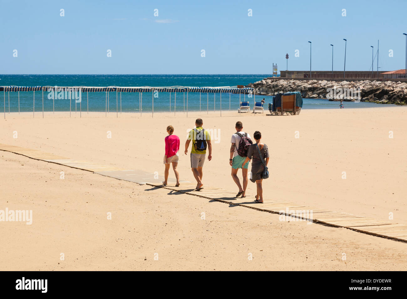 Four people walking down slatted wood access ramp to beach at Cambrils in Spain. Stock Photo