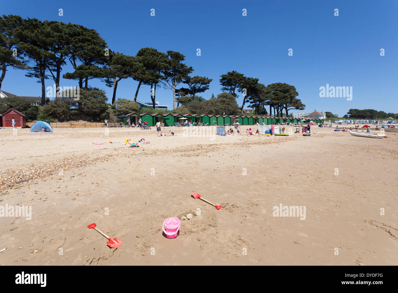 Abandoned bucket and spade on Mudeford beach with pine trees and beach huts. Stock Photo