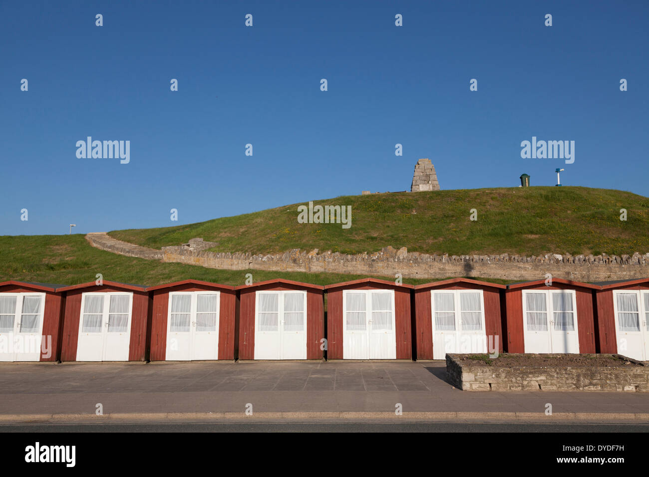 White doored beach huts on Swanage beach in front of war memorial on the hill. Stock Photo