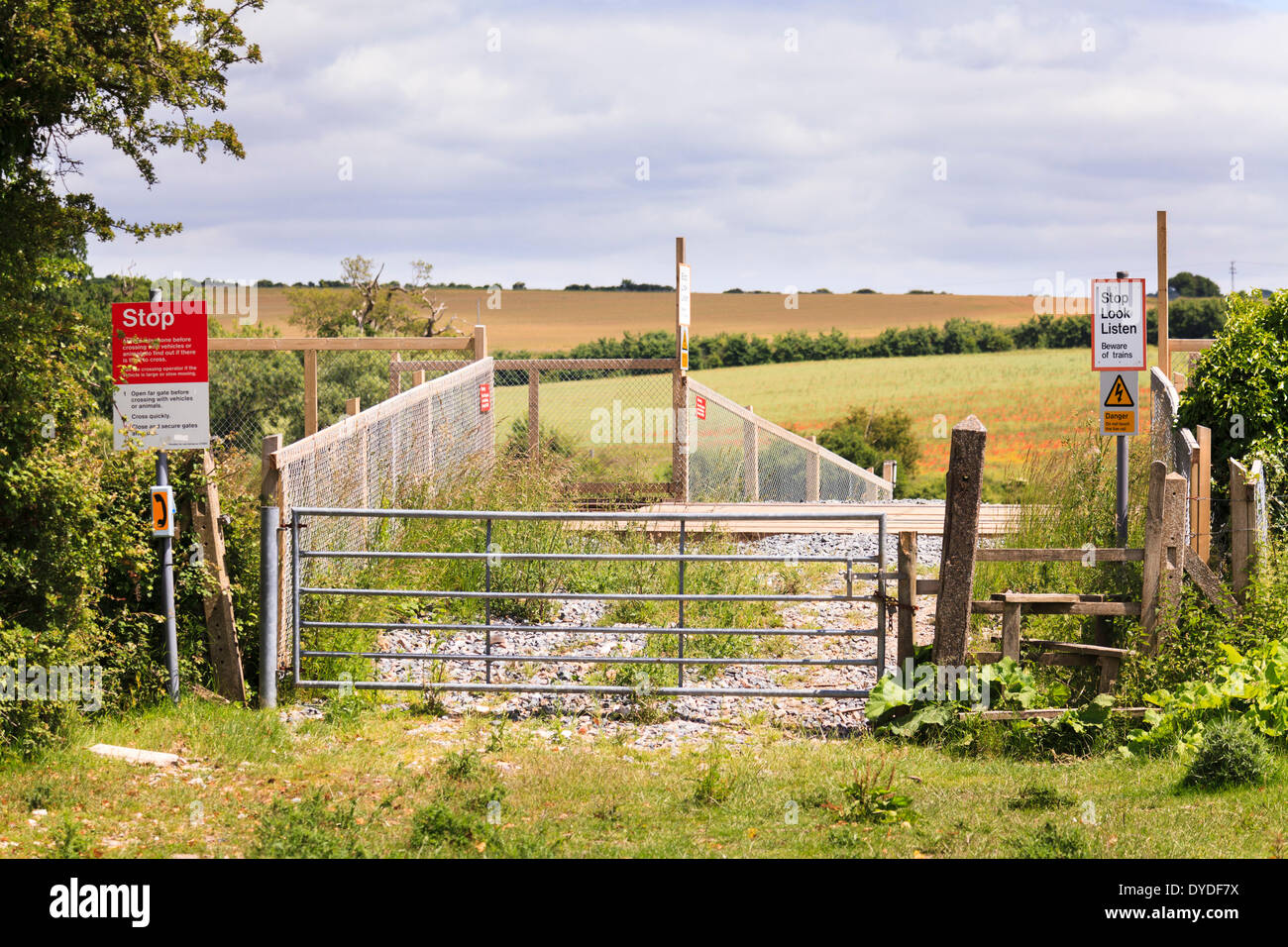Unmanned pedestrian and farm railway crossing with stile and warning signs. Stock Photo