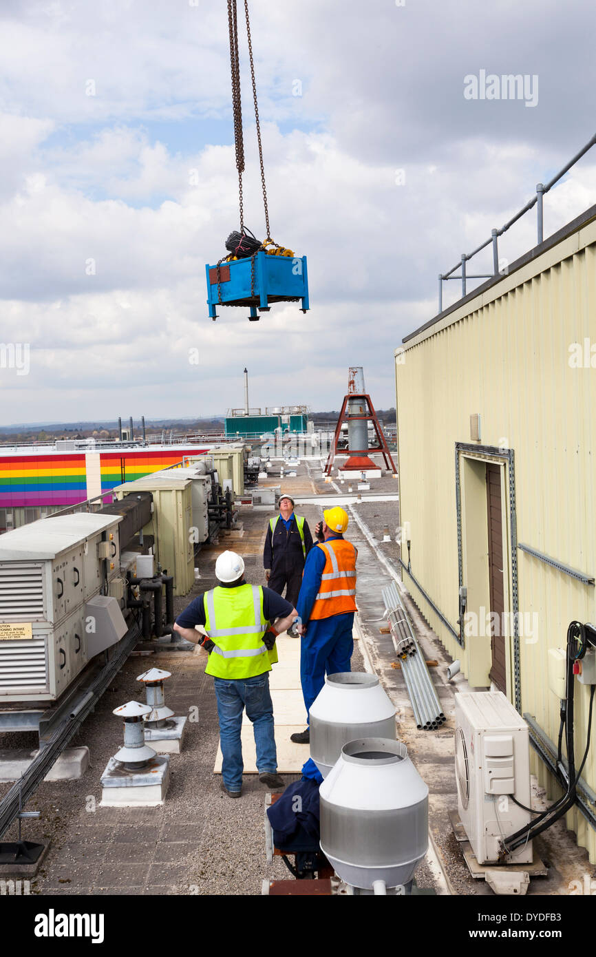 Three workman in high visibility jackets and hard hats guiding crane lift onto roof. Stock Photo
